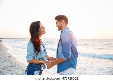 Happy young couple holding hands and laughing on the beach