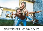 Happy young couple holding home keys after buying real estate - Husband and wife standing outside in front of their new house