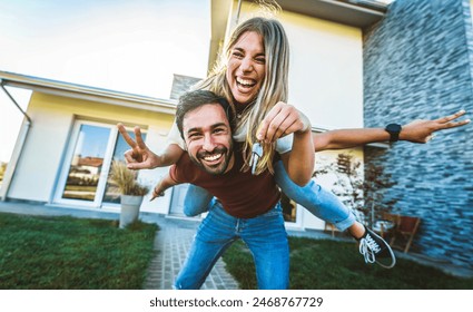 Happy young couple holding home keys after buying real estate - Husband and wife standing outside in front of their new house - Powered by Shutterstock