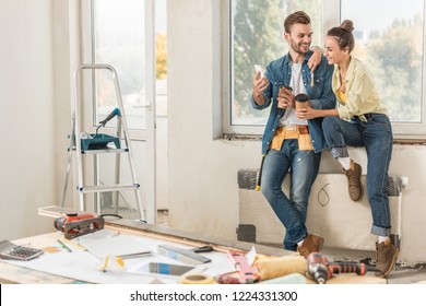 happy young couple holding paper cups and using smartphone repairment - Powered by Shutterstock