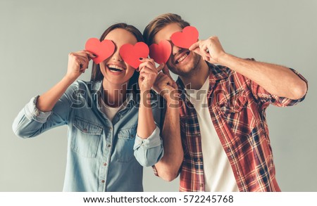 Happy young couple is holding red paper hearts and smiling, on gray background