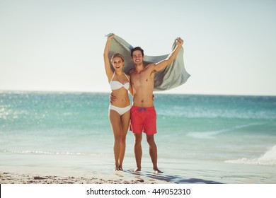 Happy Young Couple Holding Towel On Beach