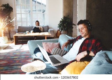 Happy young couple at home. Husband and wife sitting on the couch and watching TV series on laptop, listening music and reading books. Bright loft apartment - Powered by Shutterstock