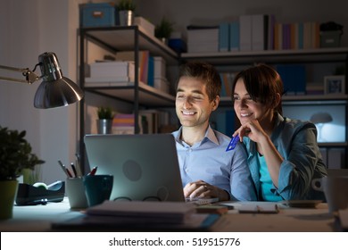 Happy Young Couple At Home Surfing The Web, Networking And Online Shopping Late At Night, She Is Holding A Credit Card