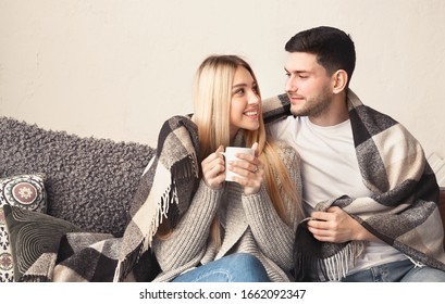 Happy Young Couple With Hot Drinks Cuddling Under Warm Blanket At Home, Empty Space