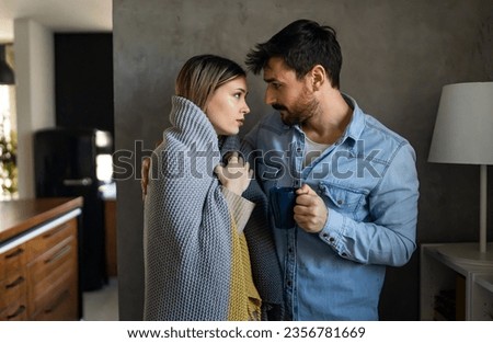 Happy young couple with hot drinks cuddling under warm blanket at home