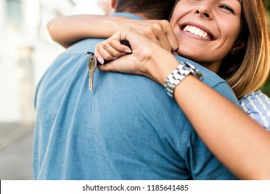 Happy Young Couple With Key In Hand Standing Outside In Front Of Their New Home.