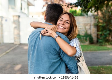 Happy Young Couple With Key  In Hand Standing Outside In Front Of Their New Home.