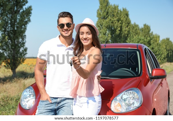 Happy\
young couple with key standing near new car on\
road