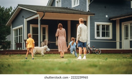 Happy Young Couple With Kids, Playing Football With A Sporty White Golden Retriever. Cheerful People Playing Ball With Pet Dog On A Lawn In Their Front Yard In Front Of The House.