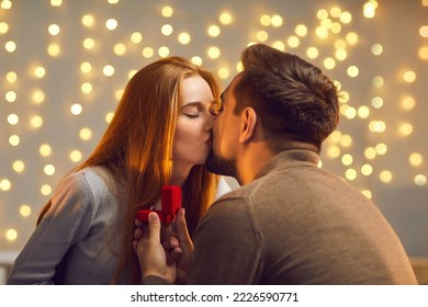 Happy young couple kissing after she said yes and accepted marriage proposal and expensive engagement ring. Man in love enjoying romantic date with his girlfriend and giving her gold jewelry