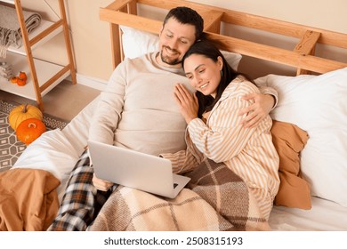 Happy young couple with laptop lying in bedroom at home on autumn day - Powered by Shutterstock