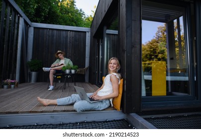 Happy Young Couple With Laptop Resting Outdoors In A Tiny House, Weekend Away And Remote Office Concept.