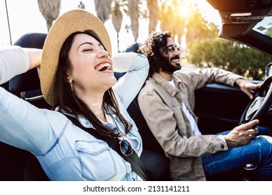 Happy young couple laughing together while driving a convertible car on holidays - Two millennial people having fun during road trip on summer vacation - Travel and rental auto service concept - Powered by Shutterstock