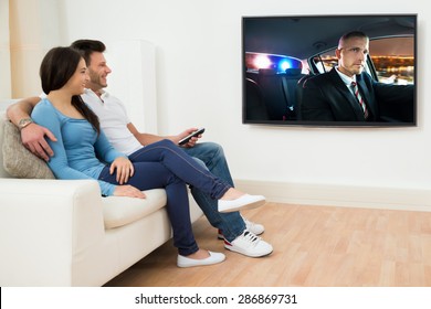 Happy Young Couple In Livingroom Sitting On Couch Watching Movie
