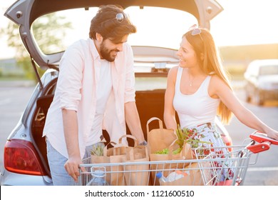 Happy young couple loading grocery bags into a car trunk at a parking lot in front of a shopping mall. - Powered by Shutterstock