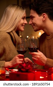 Happy Young Couple In Love Bonding, Holding Glasses, Drinking Wine, Enjoy Tender Moment Together Celebrating Valentines Day Having Romantic Dinner Date With Candles Sit At Home Table Or In Restaurant.