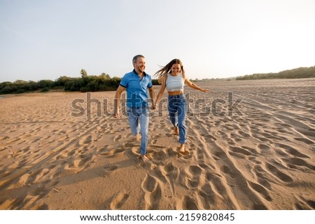 Happy young couple in love is having fun on a wild beach, running towards the sun. Rest, youth, love, lifestyle, solitude with nature. 