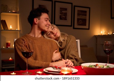 Happy Young Couple In Love Hugging, Drinking Wine, Enjoying Tender Moment Together Celebrating Valentines Day Dining At Cozy Home, Having Romantic Dinner Date With Candles Bonding Sitting At Table.