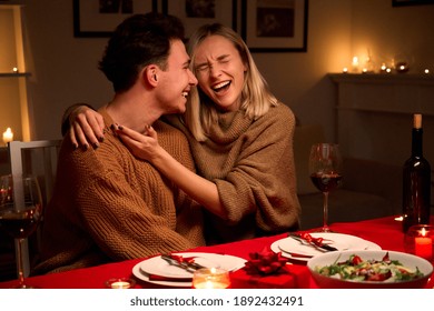 Happy Young Couple In Love Hugging, Laughing, Drinking Wine, Enjoying Talking, Having Fun Together Celebrating Valentines Day Dining At Home, Having Romantic Dinner Date With Candles Sitting At Table.