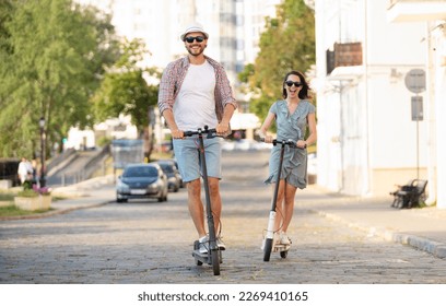 Feliz pareja joven enamorada de vacaciones divirtiéndose, conduciendo moto eléctrica por la ciudad. Transporte ecológico. Concepto de aventura y vacaciones