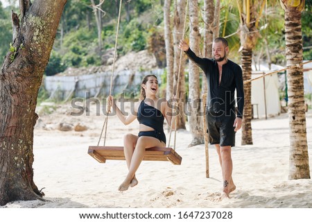 Happy young couple in love swaying on tree swing on beautiful beach and enjoying honeymoon vacation