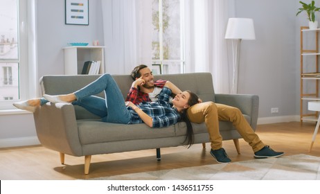 Happy Young Couple Is Lying On A New Couch In The Living Room And Having A Rest. Bright Modern Apartment With Stylish Furniture.