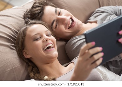 Happy young couple lying on the bed in a bedroom and using digital tablet. - Shutterstock ID 171920513