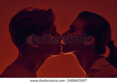 Happy young couple, man and woman kissing, smiling against red background in neon light. Monochrome. Concept of romance, love, relationship, passion, youth, dating, happiness