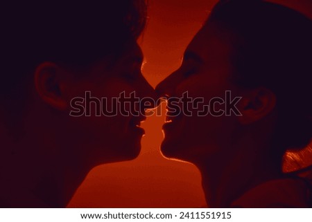 Happy young couple, man and woman kissing, smiling against red background in neon light. Monochrome. Concept of romance, love, relationship, passion, youth, dating, happiness