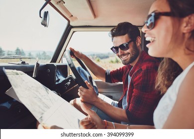 Happy young couple with a map in the car. Smiling man and woman using map on roadtrip.