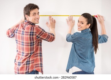 Happy Young Couple Is Measuring Their New Empty Apartment. Repair And Building Concept.