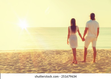 Happy Young Couple Meets Sunset On A Tropical Beach. Lovers In Full Body Length On Beach. Back Rear View 