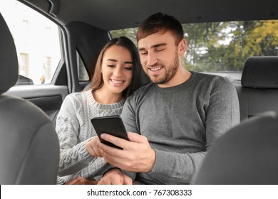 Happy Young Couple With Mobile Phone On Back Seat Of Taxi Car