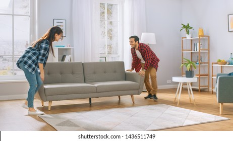 Happy Young Couple Moving New Couch into the Living Room. Bright Modern Apartment with Stylish Furniture.