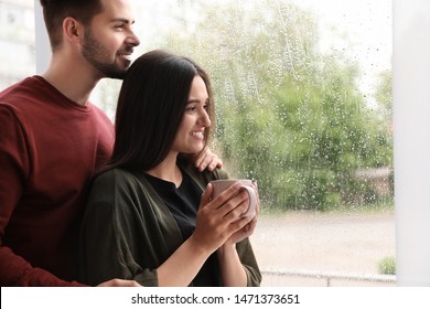 Happy Young Couple Near Window Indoors On Rainy Day