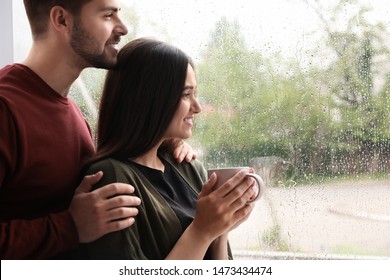 Happy Young Couple Near Window Indoors On Rainy Day