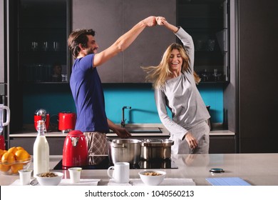 Happy Young Couple Newly Wed Dancing Listening To Music In Kitchen Wearing Pajamas Coffee Morning At Home In Love Having Fun.Concept Of: Dance, Love, Family, Happiness.