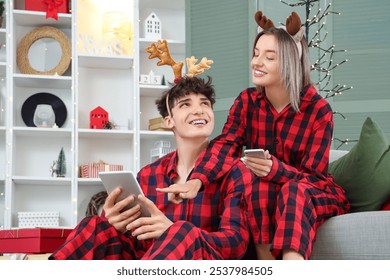 Happy young couple in pajamas with tablet computer and mobile phone shopping online at home decorated for Christmas - Powered by Shutterstock