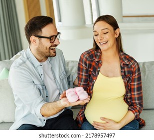 Happy young couple, pregnent woman, having fun showing small baby shoes at home - Powered by Shutterstock