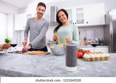 Happy Young Couple Preparing Food In Front Of Wireless Speaker In Kitchen - Powered by Shutterstock