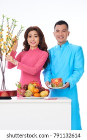 Happy young couple putting food and apricot branches on holiday dinner table