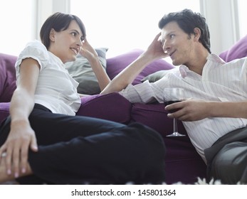 Happy young couple relaxing by sofa; man holding wineglass