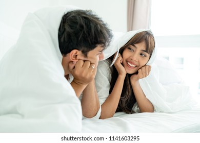 Happy young couple relaxing in home bedroom after waking up in the morning.
