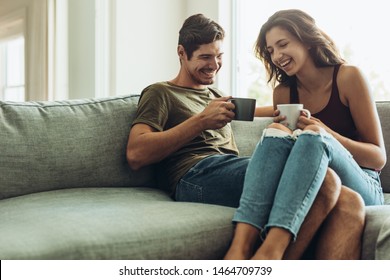 Happy young couple relaxing on couch at home with coffee. Young man and woman relaxing on sofa drinking coffee