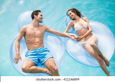 Happy Young Couple Relaxing On Inflatable Ring At Swimming Pool