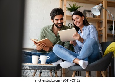 Happy Young Couple Relaxing. Reading Something On Book And Tablet Computer.