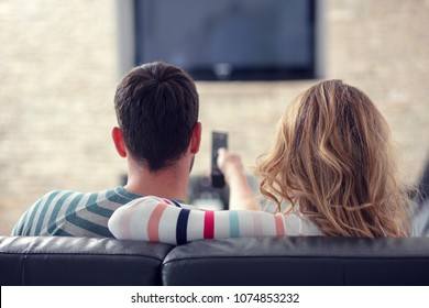 Happy young couple relaxing and watching TV at home.