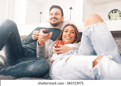 Happy young couple relaxing and watching TV at home.
