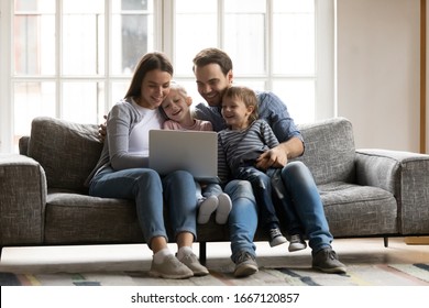 Happy Young Couple Resting With Children Siblings On Sofa, Watching Cartoons Comedian Movie On Laptop. Overjoyed Spouses Having Fun With Joyful Cute Kids Son Daughter, Using Computer At Home.